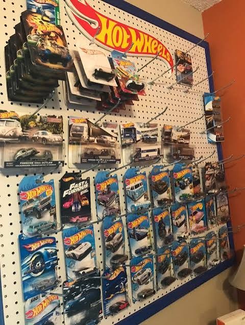 A home peg wall displaying carded Hot Wheels, including premium and mainline releases, under a Hot Wheels sign