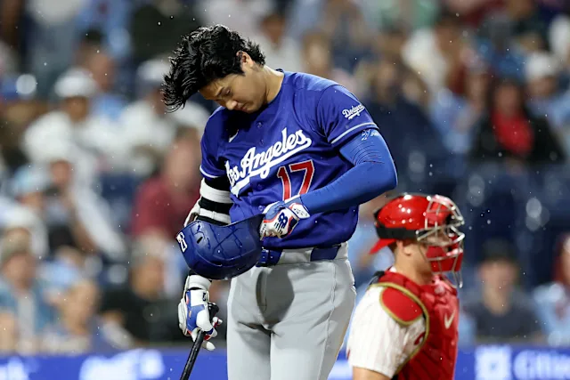 Shohei Ohtani at the plate in a Dodgers uniform, head down, adjusting his gear