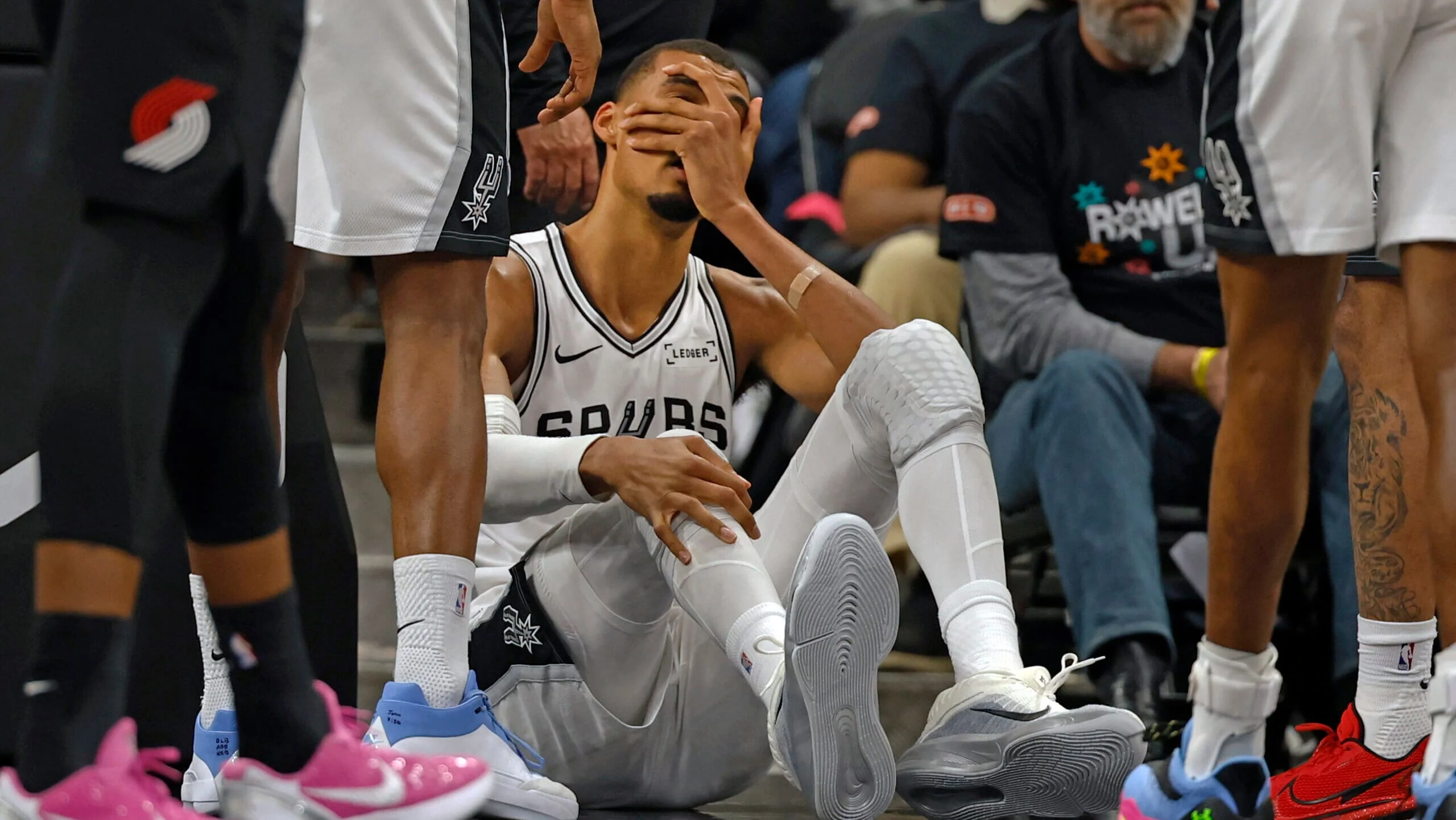 Victor Wembanyama sitting on the court with his hand covering his face